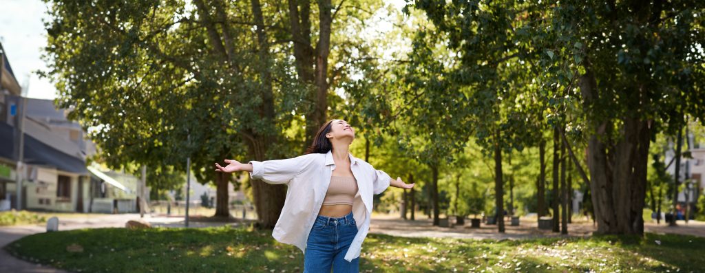 carefree asian girl dancing, feeling happiness and joy, enjoying the sun on summer day, walking in park with green trees